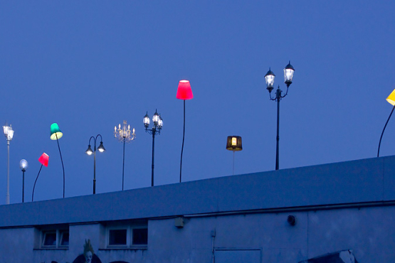 Verschiedene bunte Leuchten, montiert auf das Trambahn-Wartehäuschen am Ratzingerplatz in München in der Abenddämmerung.