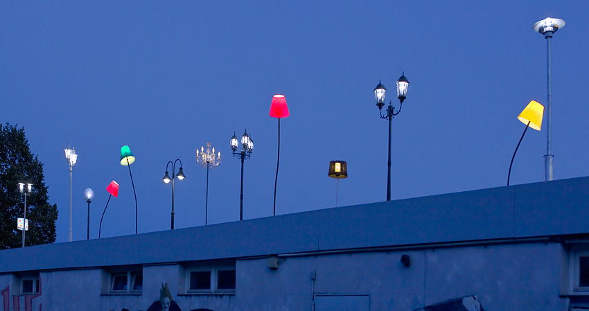 Verschiedene bunte Leuchten, montiert auf das Trambahn-Wartehäuschen am Ratzingerplatz in München in der Abenddämmerung.