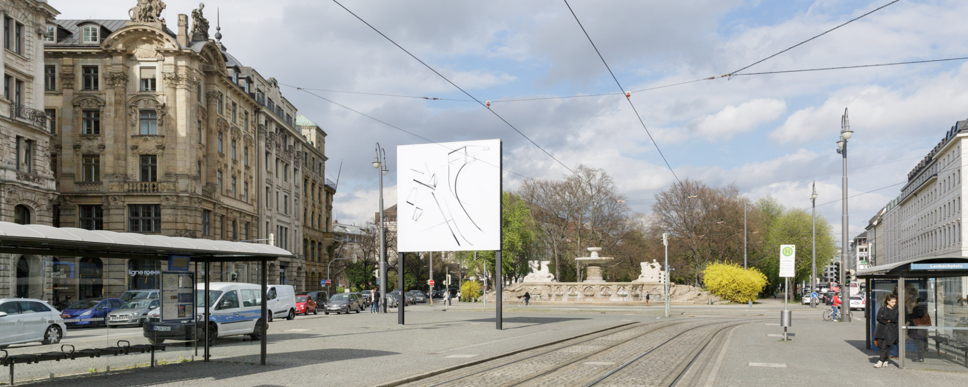 Ansicht des Lenbachplatzes Richtung stadtauswärts. Mittig das Billboard, das Motiv zeigt eine Tuschezeichnung in Schwarz-Weiß mit geometrischen und geschwungenen Formen und Linien.