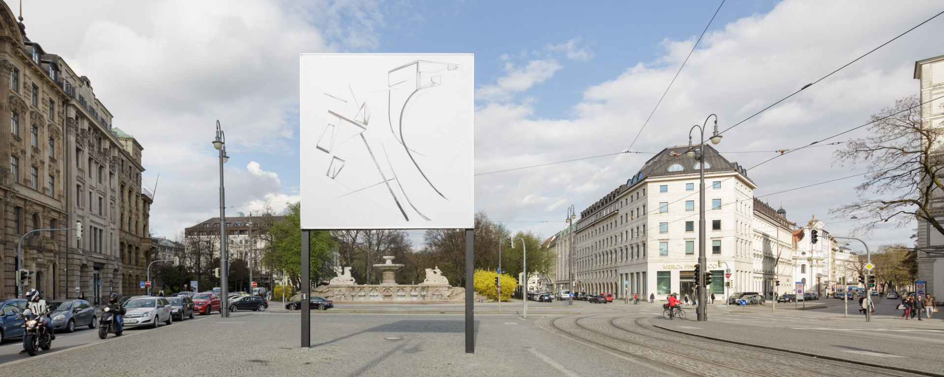View of Lenbachplatz facing out of the city. The billboard in the centre shows an ink drawing in black and white with geometric and curved shapes and lines.