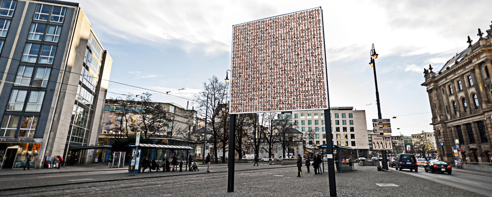 Side view of the billboard on Lenbachplatz with the motif "Israelisches Kollektivportrait" by Roland Fischer. The motif shows portraits of men and women arranged in rows, giving the impression of a collective portrait.