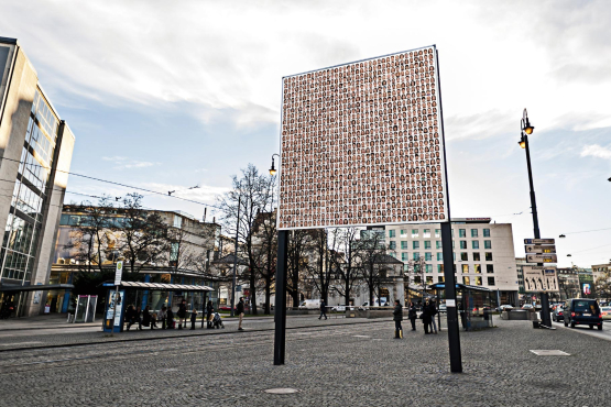 Side view of the billboard on Lenbachplatz with the motif "Israelisches Kollektivportrait" by Roland Fischer. The motif shows portraits of men and women arranged in rows, giving the impression of a collective portrait.