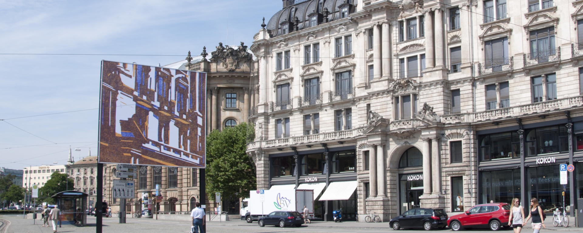 View of the billboard on Lenbachplatz looking towards the city with the motif "hide and seek" by Angela Stauber. The motif is a mirror image of the building to the right of the billboard. The architectural forms of the historic façade are simplified using the woodcut technique and abstracted into a block-like aesthetic of coloured surfaces in white, yellow and blue.