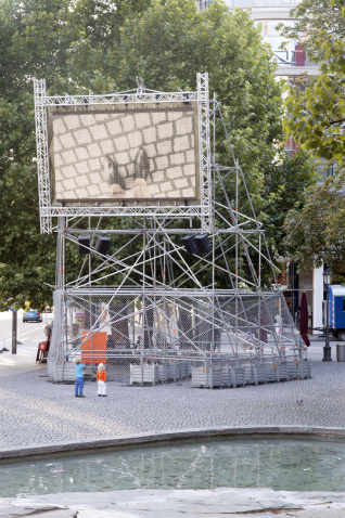 Auf dem Münchner Rindermarkt steht ein Metallgerüst mit einem aufmontierten Videoscreen, auf dem die Videoarbeit "Top View" von Nevin Aladağ gezeigt wird.