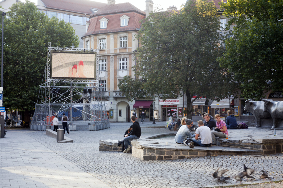 Auf dem Münchner Rindermarkt steht ein Metallgerüst mit einem aufmontierten Videoscreen, auf dem die Videoarbeit "Top View" von Nevin Aladağ gezeigt wird.