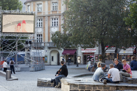 Auf dem Münchner Rindermarkt steht ein Metallgerüst mit einem aufmontierten Videoscreen, auf dem die Videoarbeit "Top View" von Nevin Aladağ gezeigt wird.