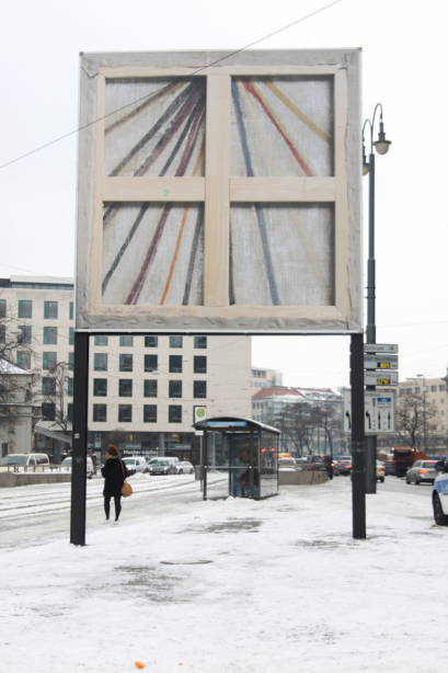Ansicht der Rückseite des Billboards am schneebedeckten Lenbachplatz. Das Motiv zeigt die Rückseite eines Keilrahmenbildes mit den Holzkeilen. Die abstrakte farbige Komposition der Vorderseite scheint auf der Rückseite der Leinwand durch.