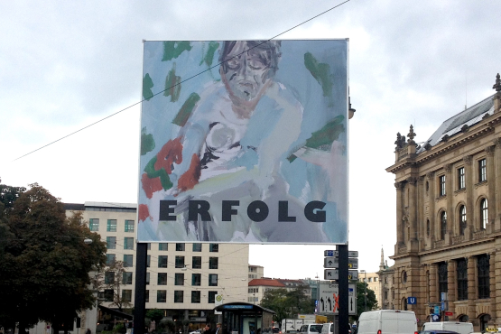 Frontal view of the billboard at Lenbachplatz photographed towards the city centre. The billboard features a work by the artist Stephan Dillemuth. The motif shows an abstract portrait of a naked man against a blue-green background. The word "Erfolg" (success) is written in bold black capital letters in the lower third of the image.