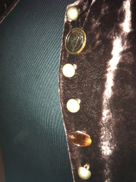 Close-up of a woman wearing a shiny brown jacket. Between the round buttons of the jacket are two coins instead of buttons - a 1 euro coin and a 5 cent coin.