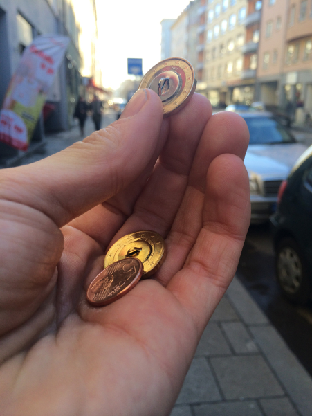 Photo of a hand holding three coins - a 1 euro coin, a 20 cent coin and a 5 cent coin. All the coins have been converted into buttons on the reverse.