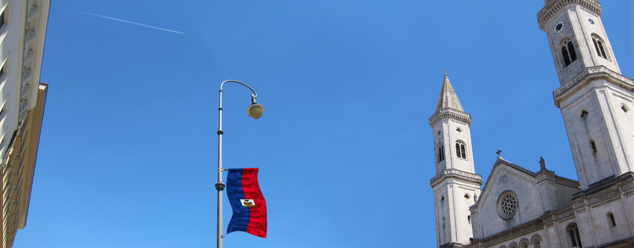 View of a street lamp on Ludwigstraße, photographed from below. As part of an art installation by artist Silke Witzsch, the national flag of Haiti is attached to the street lamp at half height. The flag has been artistically distorted by placing a camouflage pattern over the national flag.