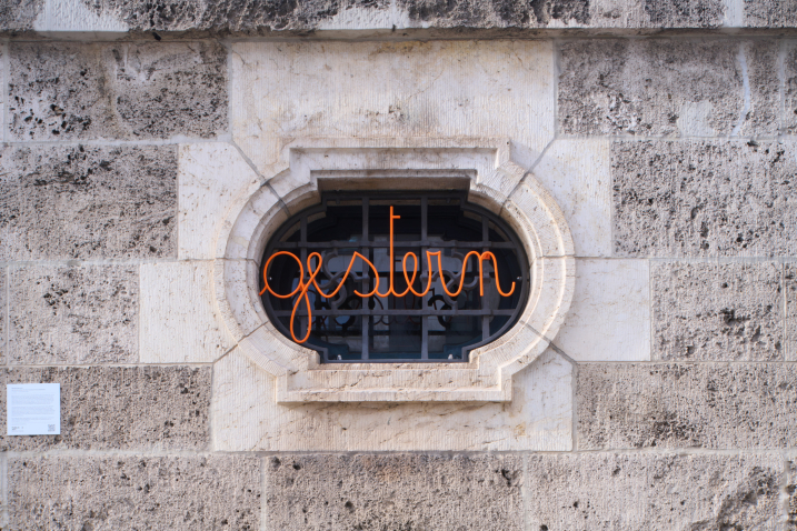 You can see a house wall with a window grille. In this window grille is a swastika pattern, in front of which is the curved orange lettering ‘gestern’.