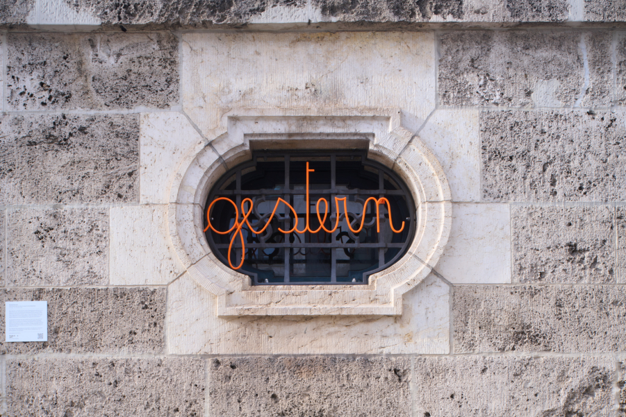 You can see a house wall with a window grille. In this window grille is a swastika pattern, in front of which is the curved orange lettering ‘gestern’.