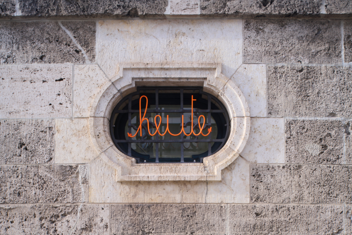 The image shows a house wall with a window grille. The grille features a swastika pattern, and in front of it is the curved orange lettering "today."