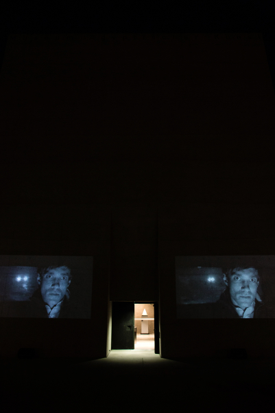 Photograph of a double video projection of the film "Wednesday" by the artist duo M+M on the outer façade of the entrance gate of the State Museum of Egyptian Art. The black-and-white video stills on display show the same man in frontal view, driving in a car in the dark. His expression is serious. The headlights of another car can be seen through the rear window.