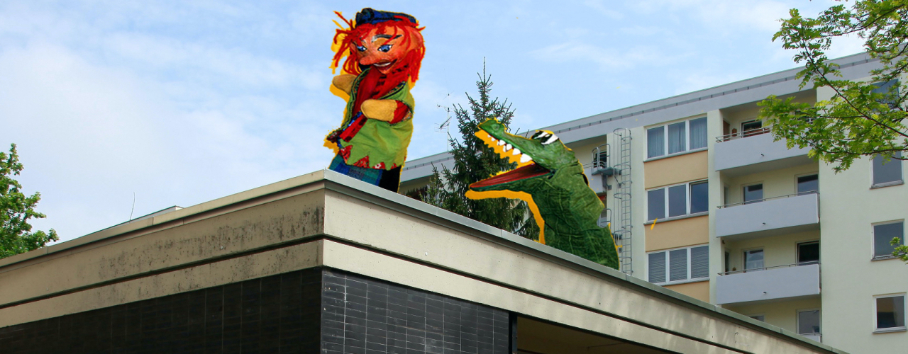 The picture shows a photo collage. A single-storey building can be seen in the foreground and a multi-storey apartment block in the background. A punch and a hand puppet crocodile figure are retouched onto the roof of the single-storey house, performing a kind of Punch-and-Judy-show on the roof.