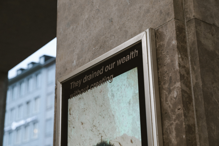 Detailaufnahme eines Bildschirms an einer Steinwand mit dem Text ‚They drained our wealth without creating‘.
