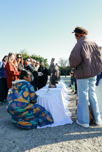 Gruppe von Menschen steht im Freien um einen mit weißen Tüchern bedeckten Tisch mit Skulpturen.