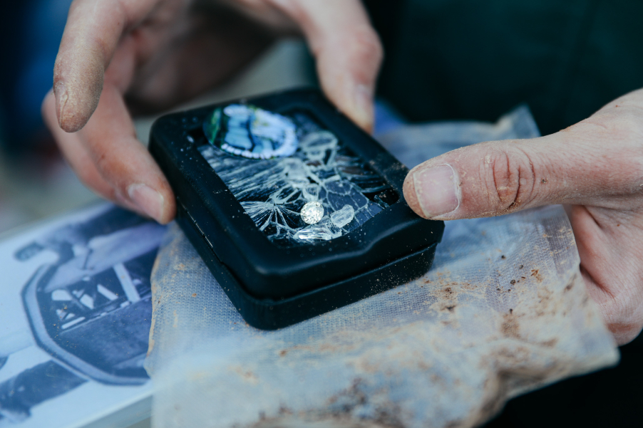 schmutzige Hände halten ein schwarzes Kästchen, darauf liegend ein Diamant