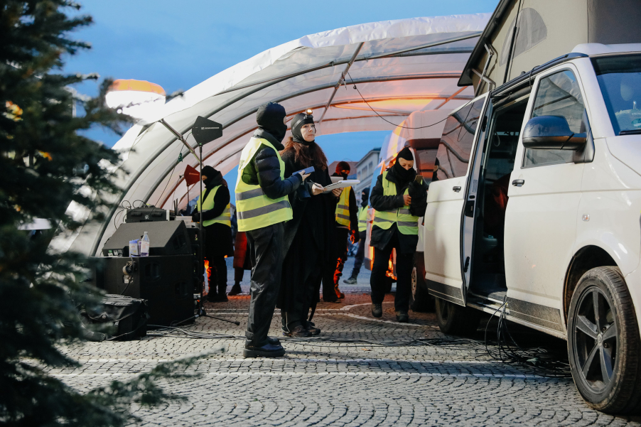 Mehrere, teilweise vermummte Personen in Warnwesten arbeiten an einer mobilen Station neben einem weißen Transporter unter einem Zelt.