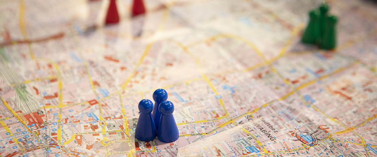 Bunte Spielfiguren (blau, rot, grün) stehen auf einem Stadtplan.