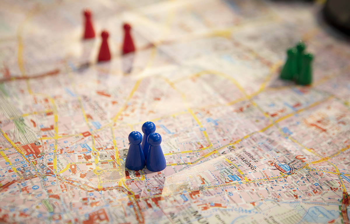 Bunte Spielfiguren (blau, rot, grün) stehen auf einem Stadtplan.