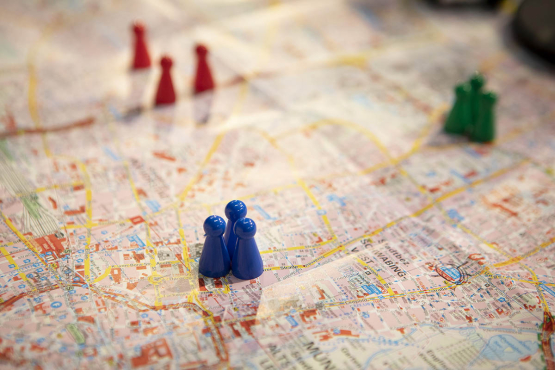 Bunte Spielfiguren (blau, rot, grün) stehen auf einem Stadtplan.