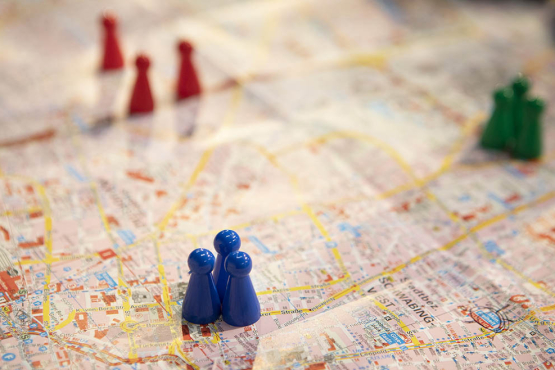 Bunte Spielfiguren (blau, rot, grün) stehen auf einem Stadtplan.