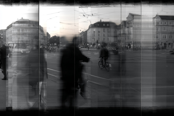 Schwarz-Weiß-Foto auf einem Filmstreifen: Verschwommene Menschen und ein Fahrradfahrer auf einem belebten Stadtplatz mit alten Gebäuden.