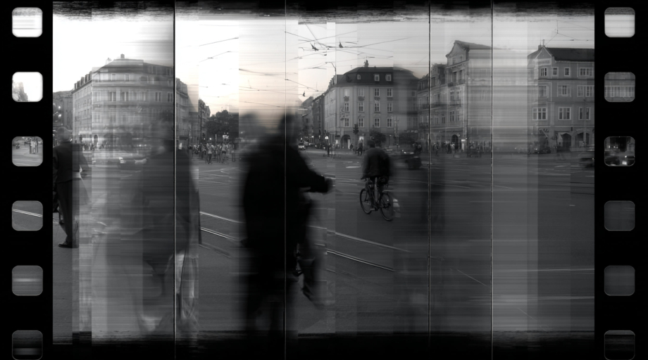 Schwarz-Weiß-Foto auf einem Filmstreifen: Verschwommene Menschen und ein Fahrradfahrer auf einem belebten Stadtplatz mit alten Gebäuden.