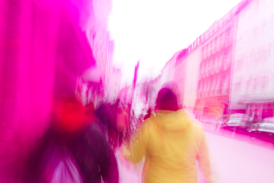A blurred image shows people walking on the sidewalk from behind. There are building facades on the left and right. The image is overlaid with a red transparent layer.