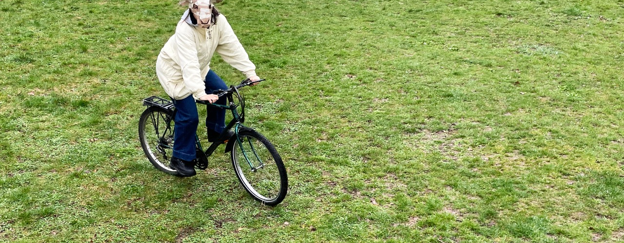 Person mit Schafsmaske fährt Fahrrad über eine Wiese.