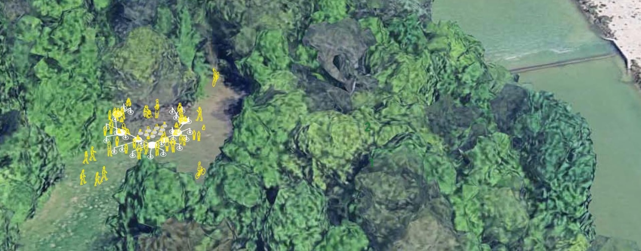 An aerial view of a river with gravel banks and paths along the banks, surrounded by forest. Small yellow figures are marked on the left bank.